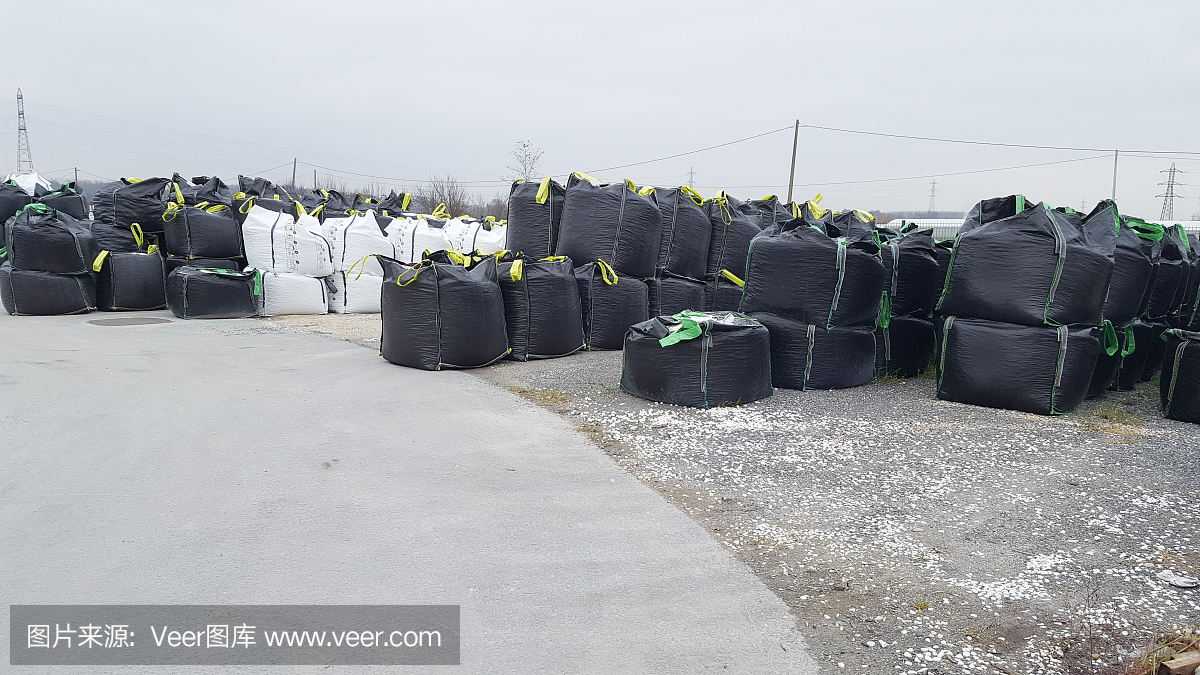 开放式仓库的大黑色堆垛散货在大袋仓库中储存,用于配送进出口物流业务